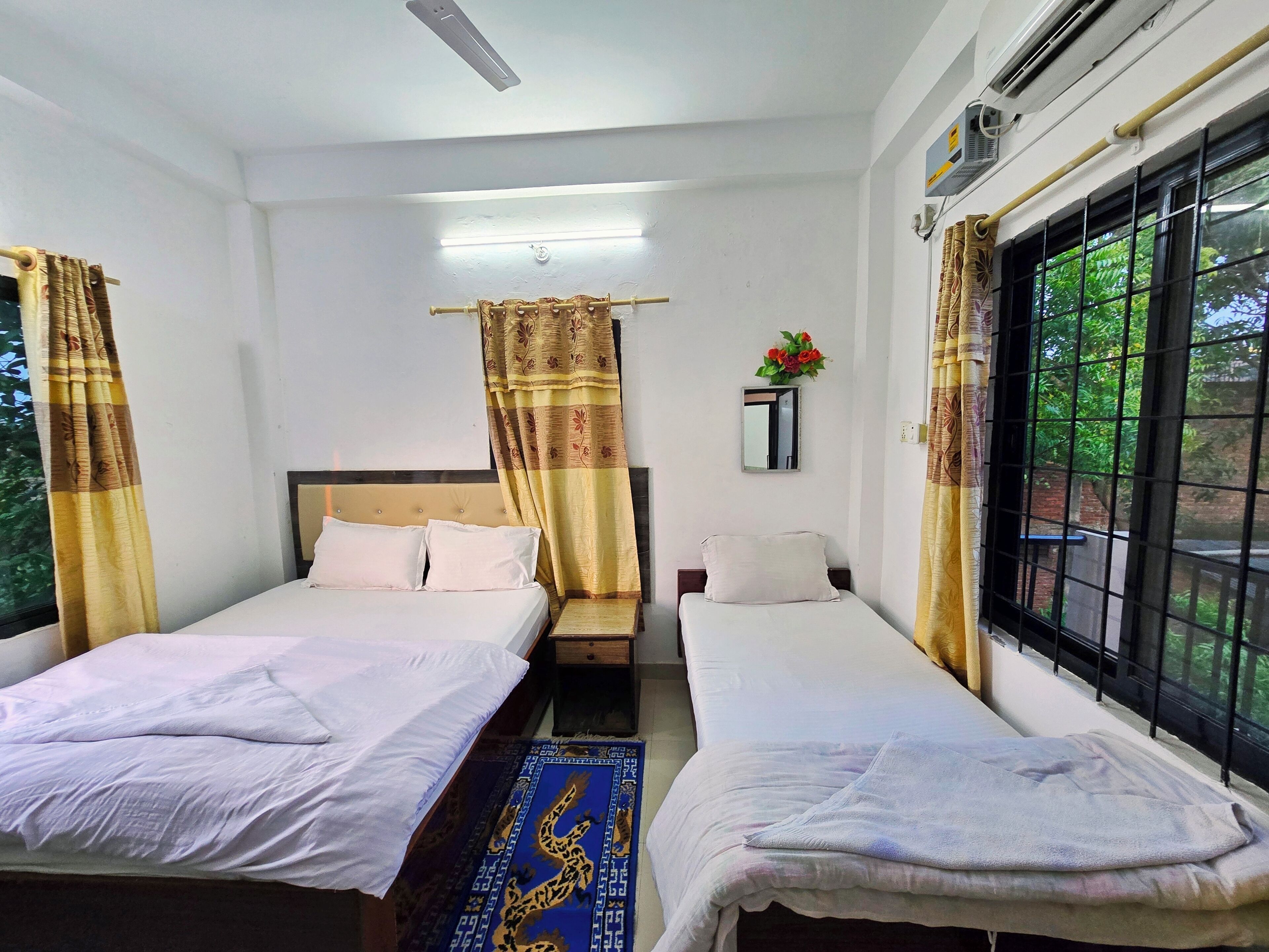 Habitación de hotel con dos camas, un espejo, una ventana que da a zonas verdes y un equipo de aire acondicionado.