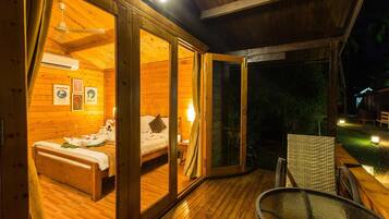 A wooden cabin with a bed, a small table, and a glass door leading to an outdoor area.