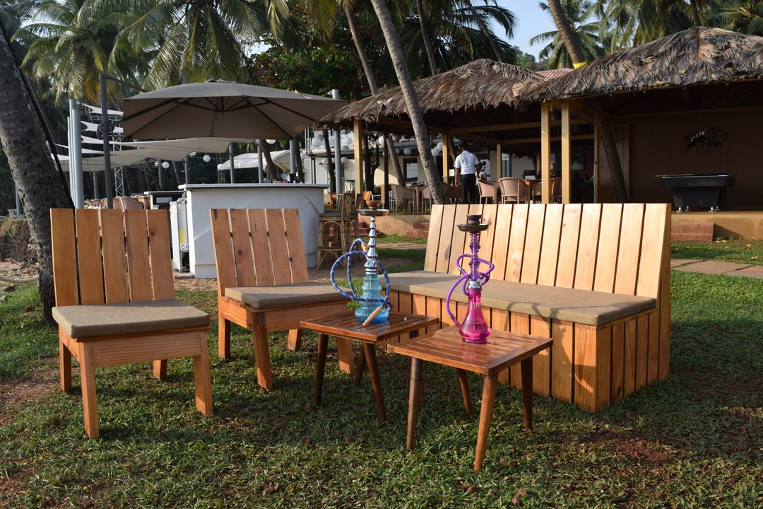 Un espace extérieur aménagé avec du mobilier en bois, comprenant des chaises et un banc, ainsi qu’une table sur laquelle est posé un narguilé.