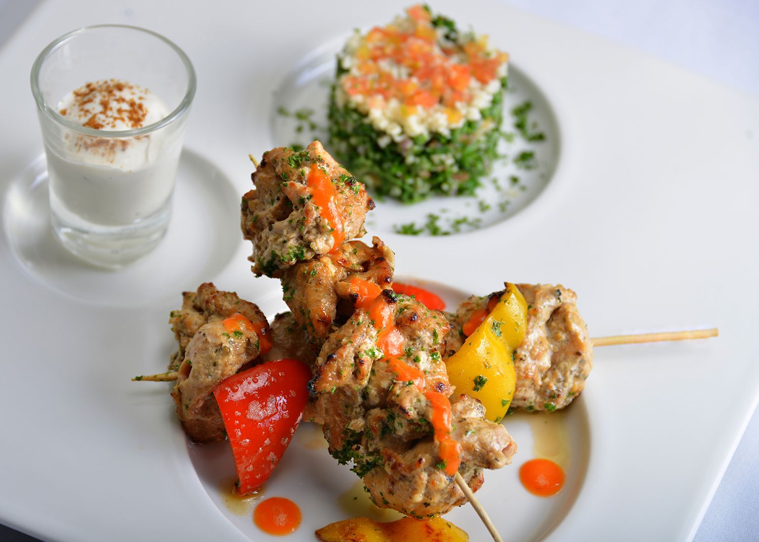 A plate of skewered meat with vegetables and a glass of a creamy beverage.