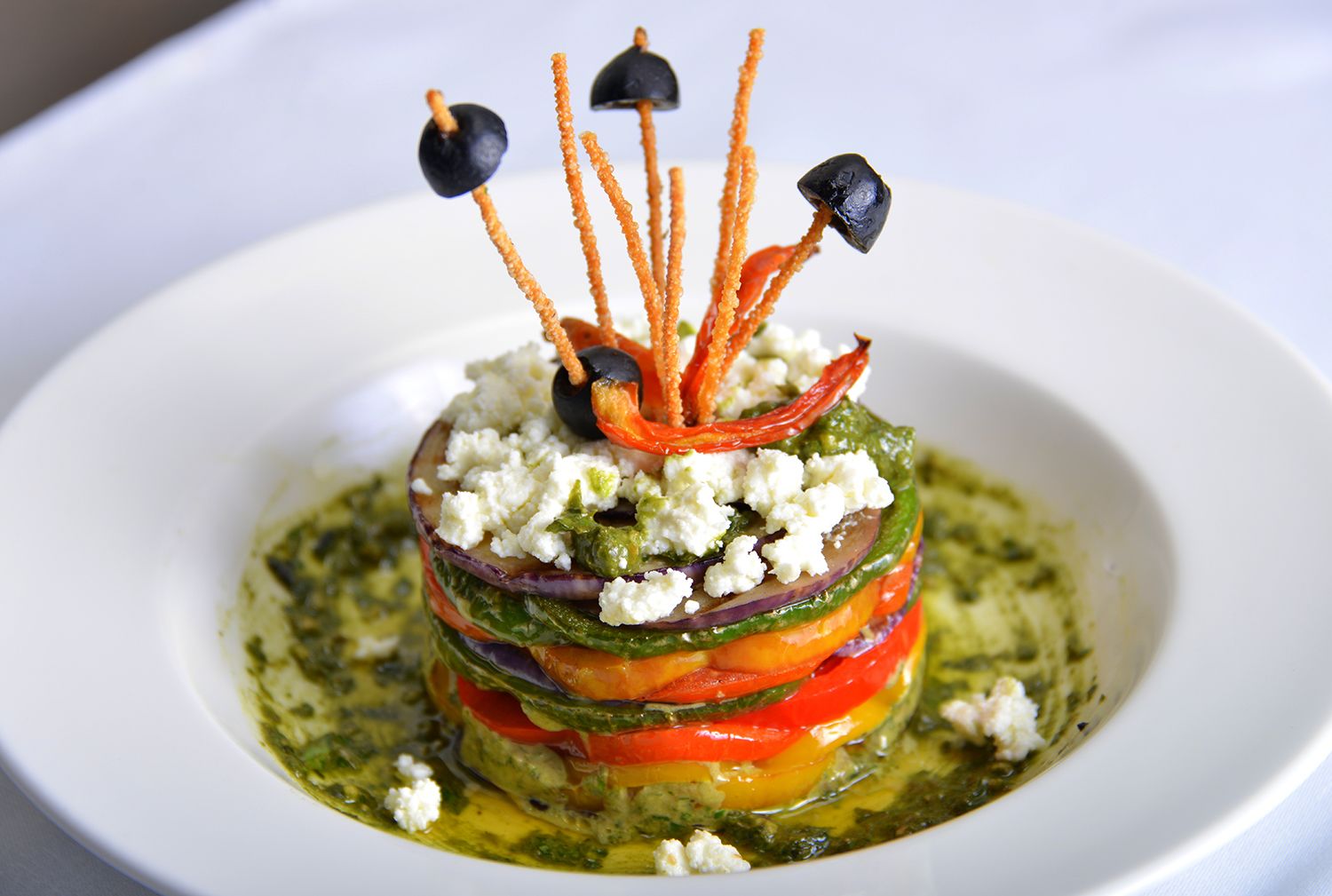 A layered vegetable and cheese dish with a decorative garnish on a white plate.