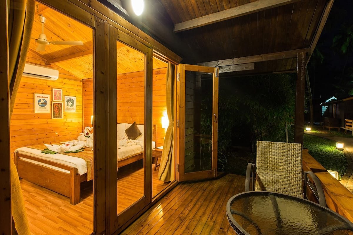 Uma cabana de madeira com cama, uma mesinha e uma porta de vidro para o exterior.