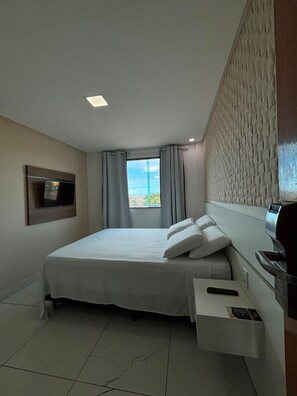 Une chambre d’hôtel avec un lit, un téléviseur fixé au mur, une fenêtre avec des rideaux et une vue sur l’extérieur.