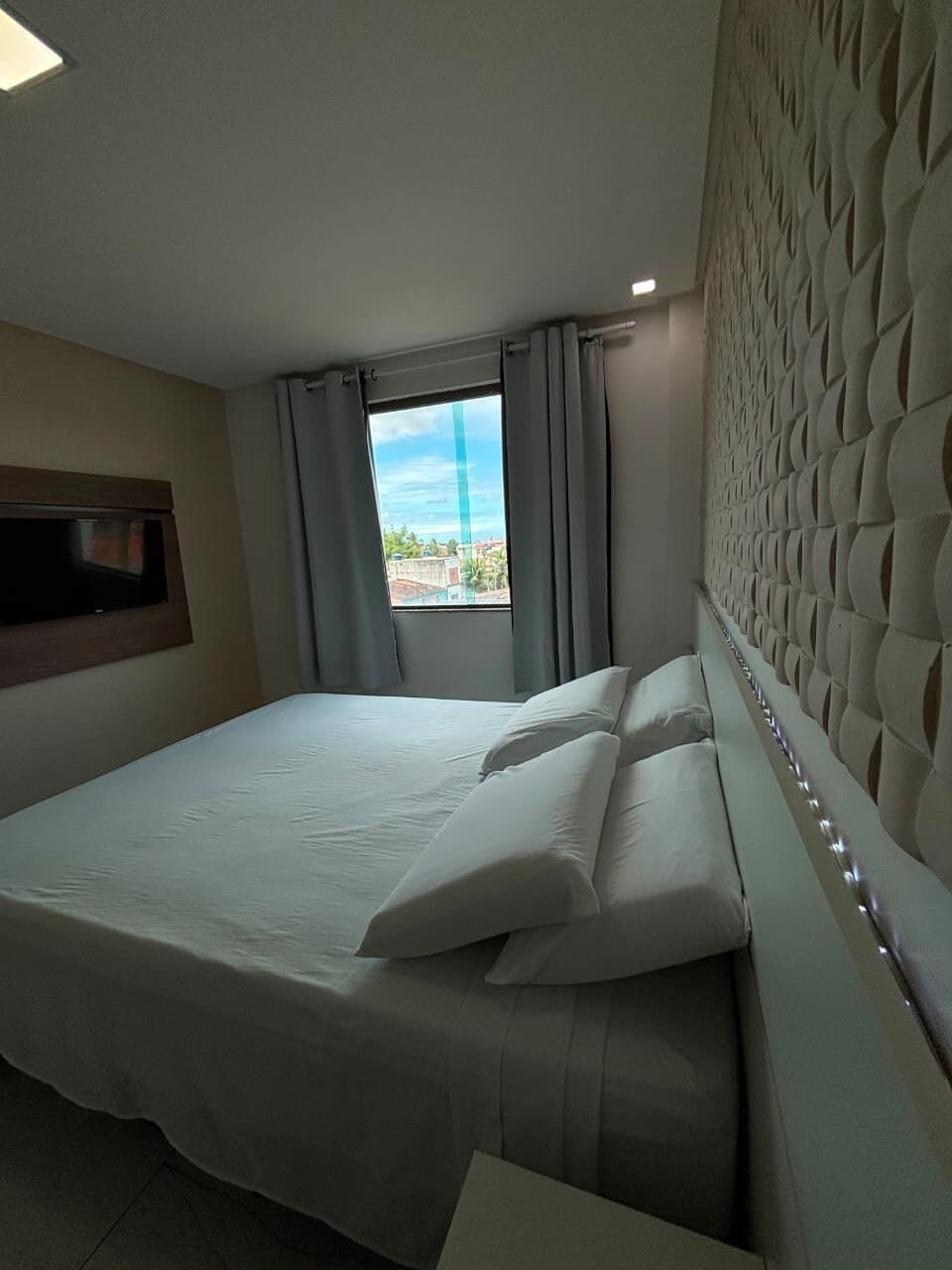 Habitación de hotel con una cama grande, un televisor en la pared y vistas a la ciudad por la ventana.