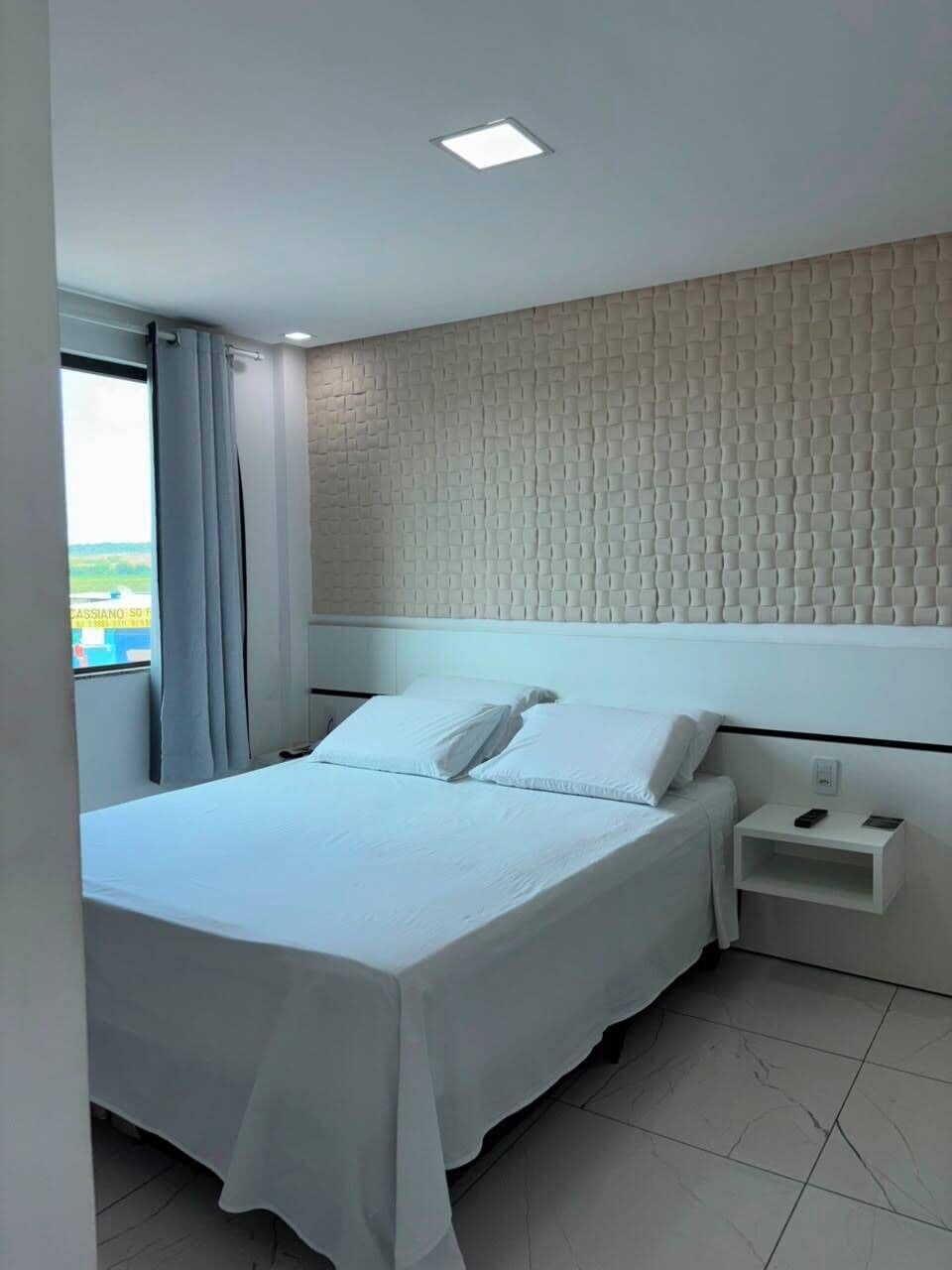 Habitación de hotel con cama, mesita de noche, ventana con cortinas y pared con textura.