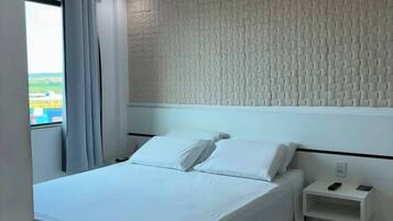 Habitación de hotel con cama, mesita de noche, ventana con cortinas y pared con textura.