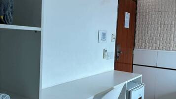 A room with a white desk, a chair, a small refrigerator, an air conditioning unit, a door, and a textured wall.