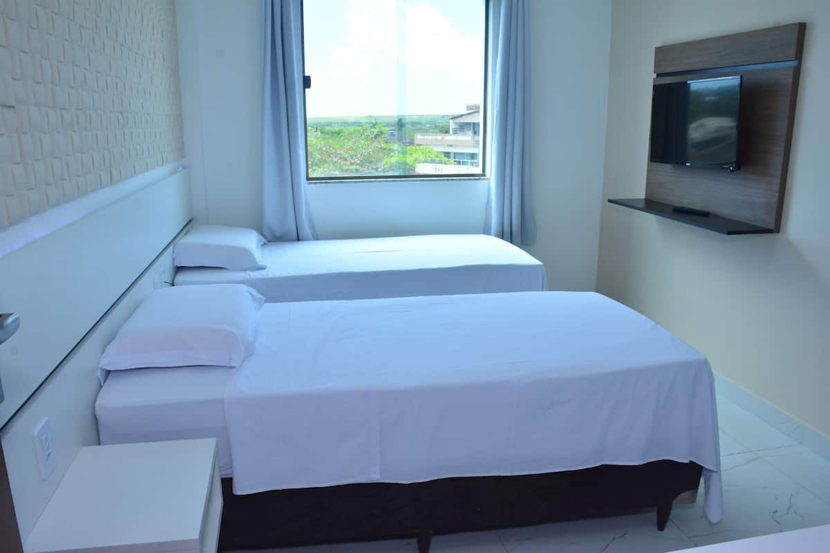 A hotel room with two beds, a TV mounted on the wall, and a window with a view.