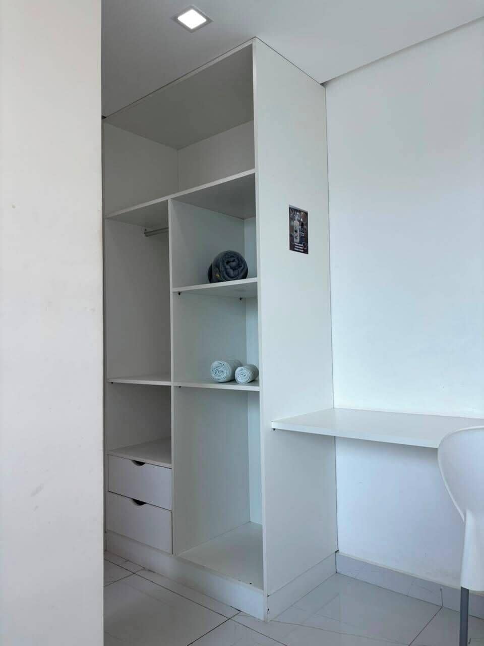 Un armario blanco con varios estantes y una pequeña zona de escritorio.