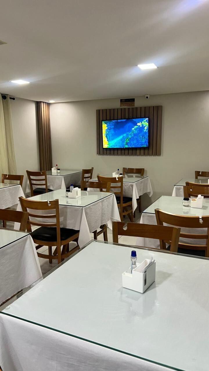 Un comedor de hotel con mesas dispuestas para los huéspedes, un televisor montado en la pared y una cámara de seguridad encima.