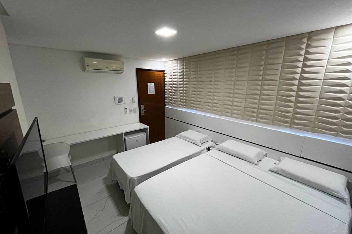 A hotel room with two beds, a small desk, a mirror, and a window with blinds.