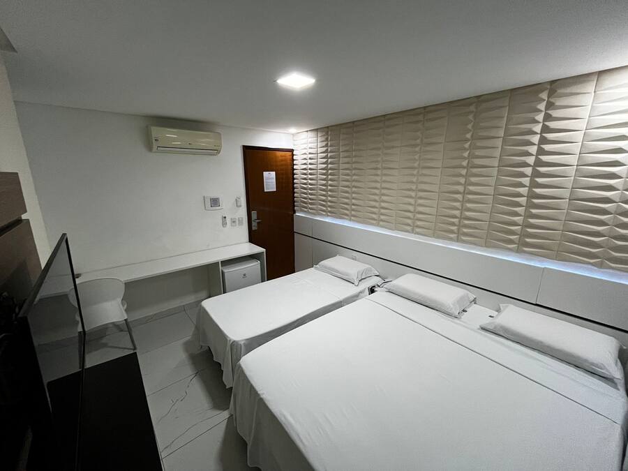 Habitación de hotel con dos camas, un escritorio pequeño, un espejo y una ventana con persianas.