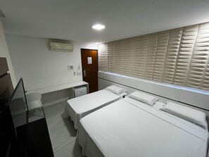 A hotel room with two beds, a small desk, a mirror, and a window with blinds. - Goiana Palace Hotel (Goiana)