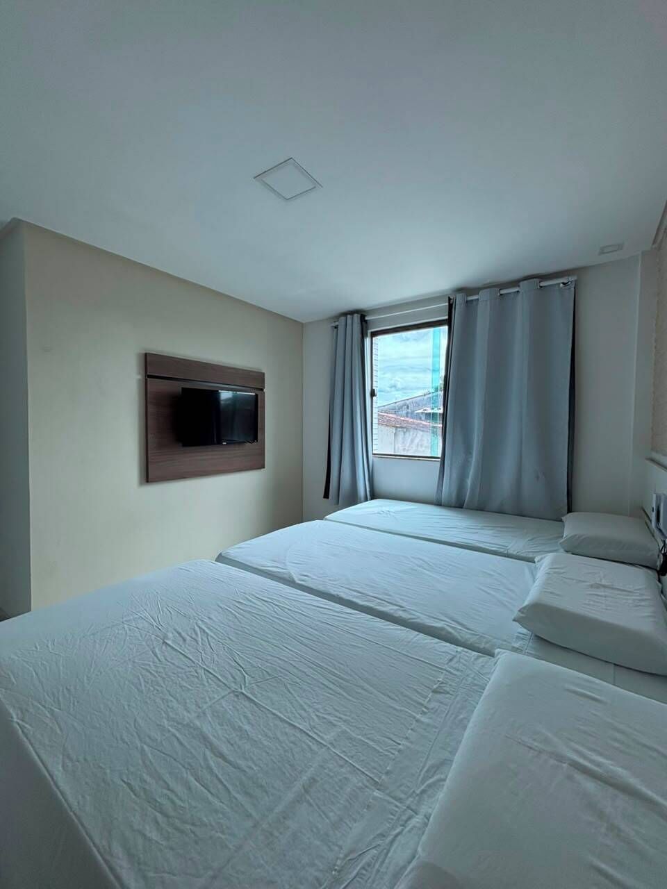 Habitación de hotel con cama, televisión montada en la pared y ventana con cortinas.