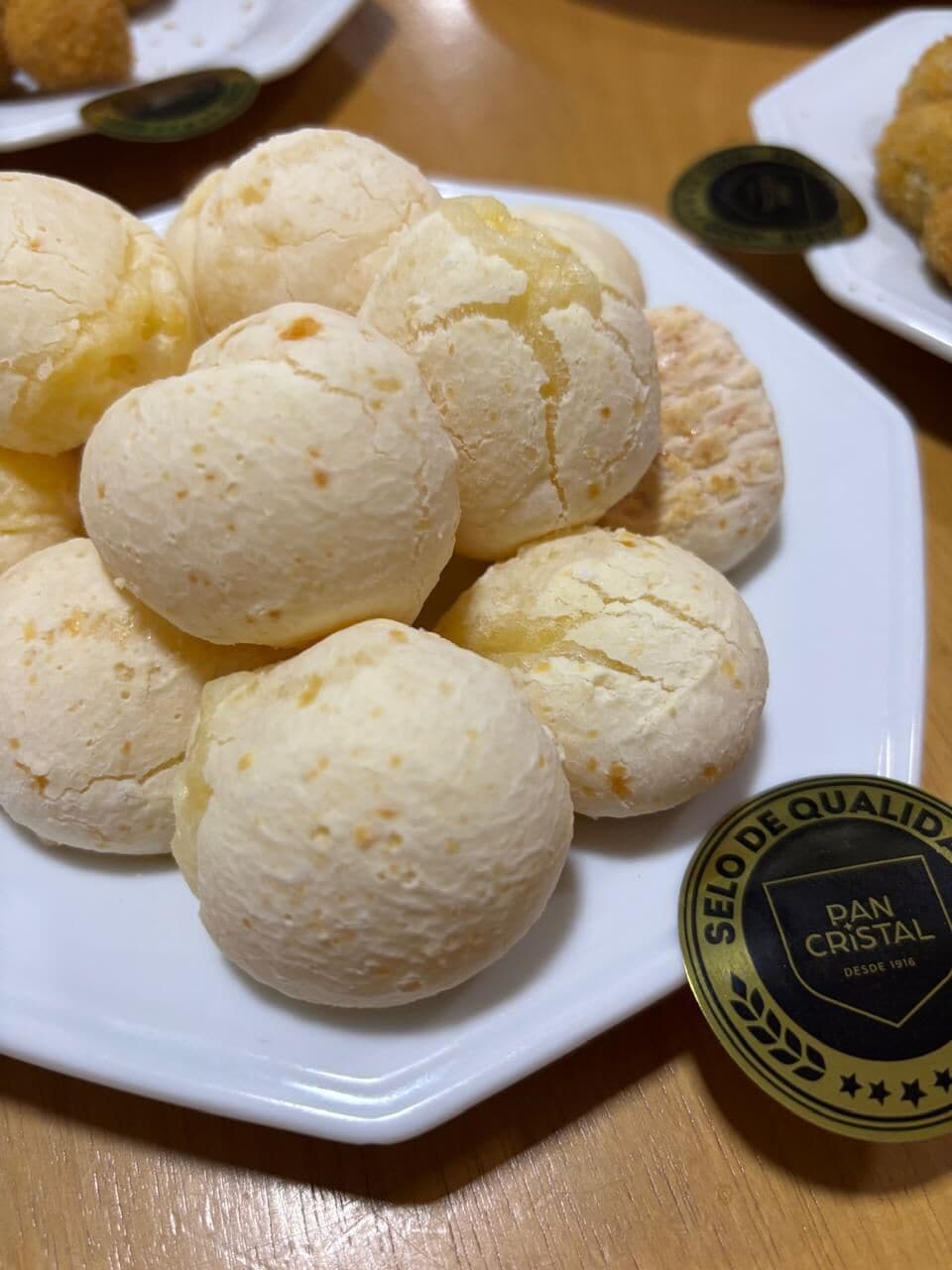 En tallrik med pão de queijo, och en etikett som lyder: ”SELO DE QUALID DAN CRISTAL DESDE 1914”.