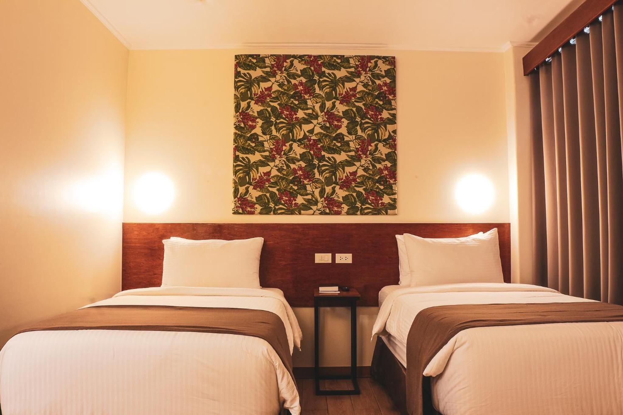 A hotel room with two beds, a wooden headboard, a wall-mounted floral artwork, and two bedside lamps.