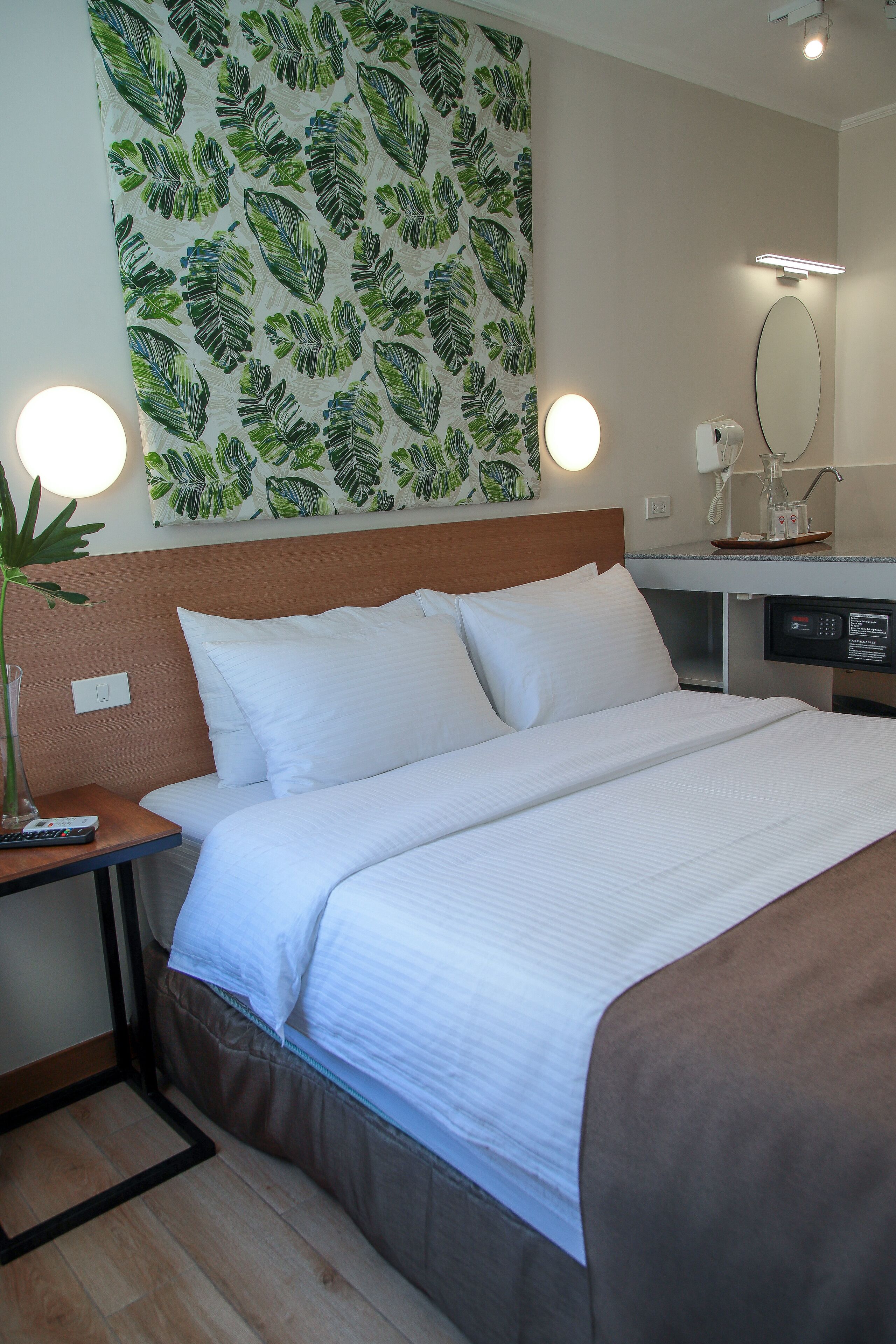 A hotel room with a bed, bedside table, lamp, and a wall with a leaf pattern.