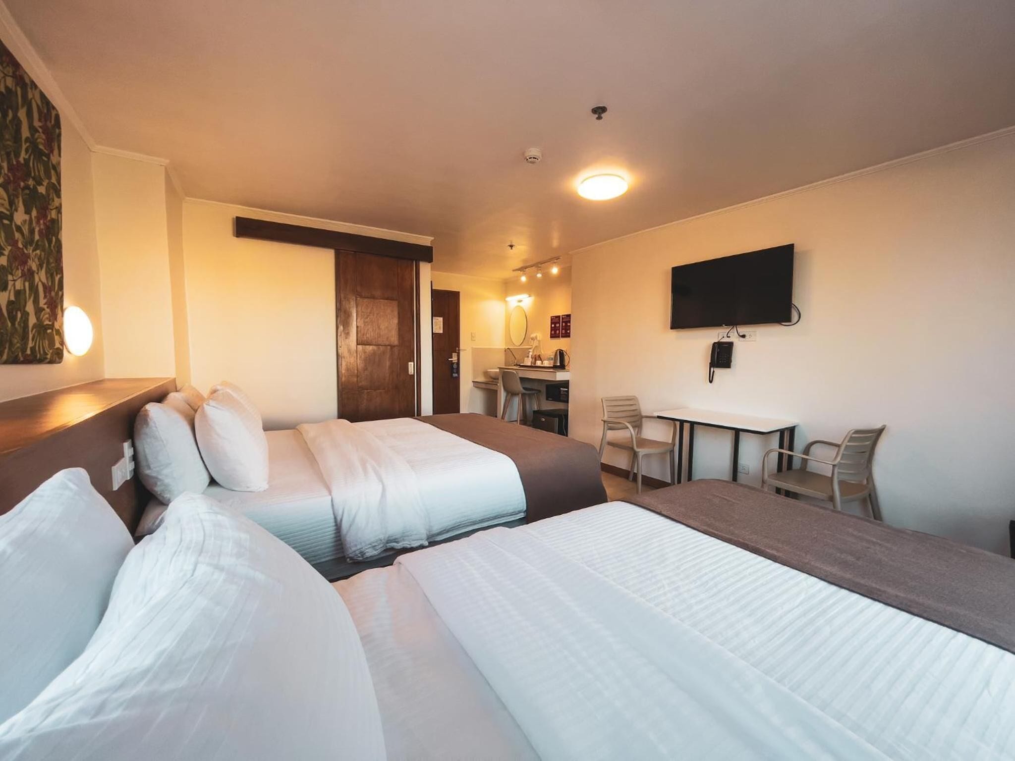 A hotel room with two beds, a desk, a chair, a TV, and a bathroom visible in the background.