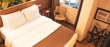 Una habitación de hotel con una cama grande, una mesita pequeña, una silla y una ventana con cortinas.