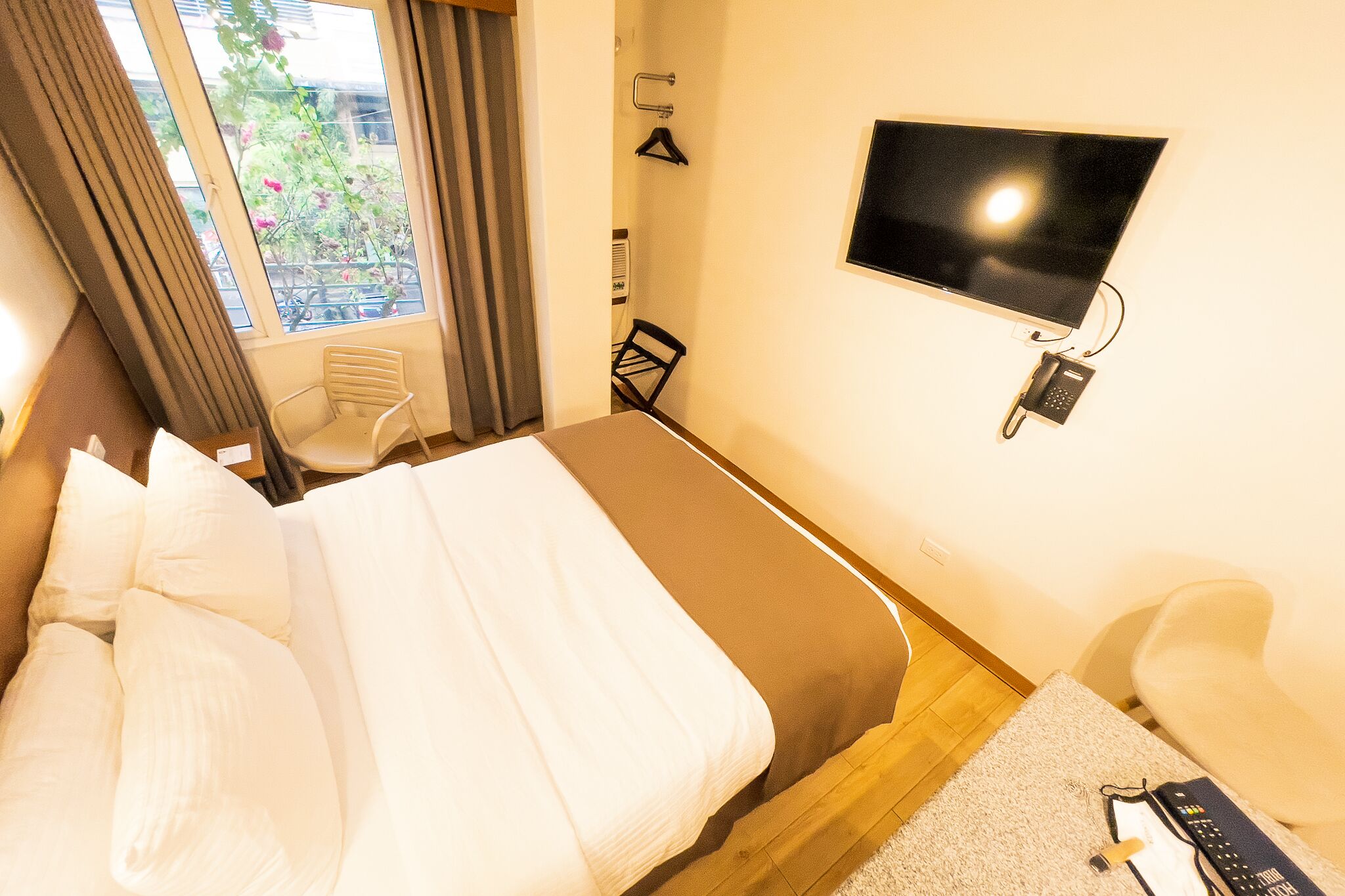 A hotel room with a bed, a TV mounted on the wall, a chair, and a small table with a remote control.