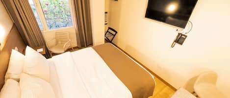 A hotel room with a bed, a TV mounted on the wall, a chair, and a small table with a remote control.
