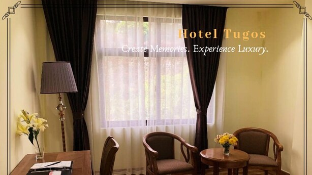 A hotel room with a bed, two armchairs, a small table, a lamp, and a window with curtains. - Hotel Tugos (Baguio)