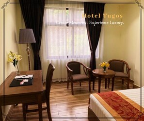 A hotel room with a bed, two armchairs, a small table, a lamp, and a window with curtains. - Hotel Tugos (Baguio)