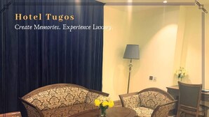 A hotel room with a dark blue curtain, a patterned sofa, two armchairs, a wooden coffee table, and a lamp. - Hotel Tugos (Baguio)