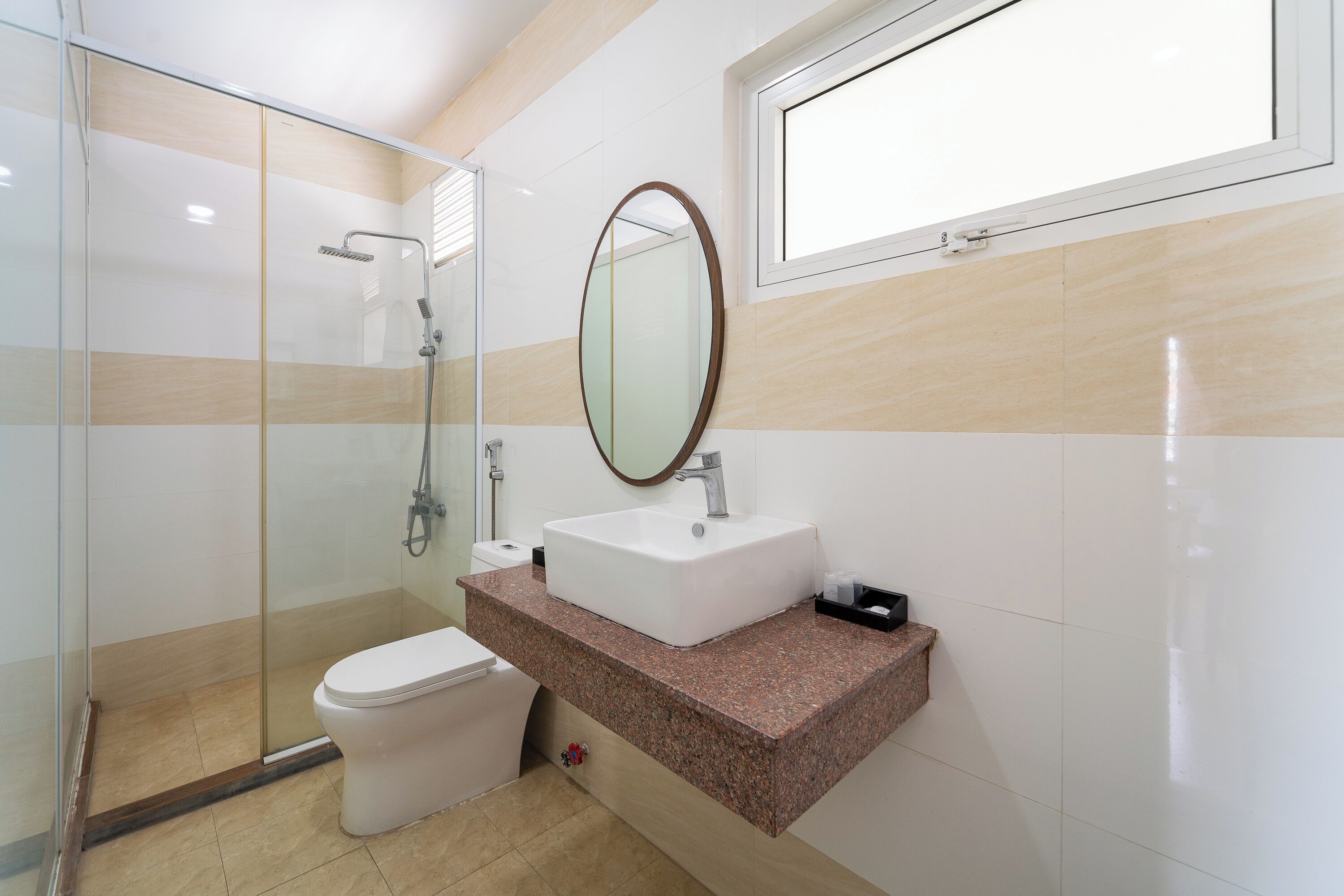 A bathroom with a glass-enclosed shower, a white toilet, a sink with a mirror, and a window above the sink.
