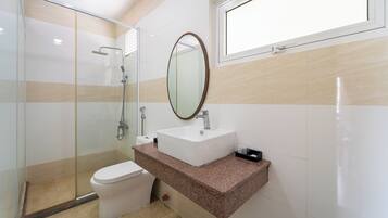 A bathroom with a glass-enclosed shower, a white toilet, a sink with a mirror, and a window above the sink.