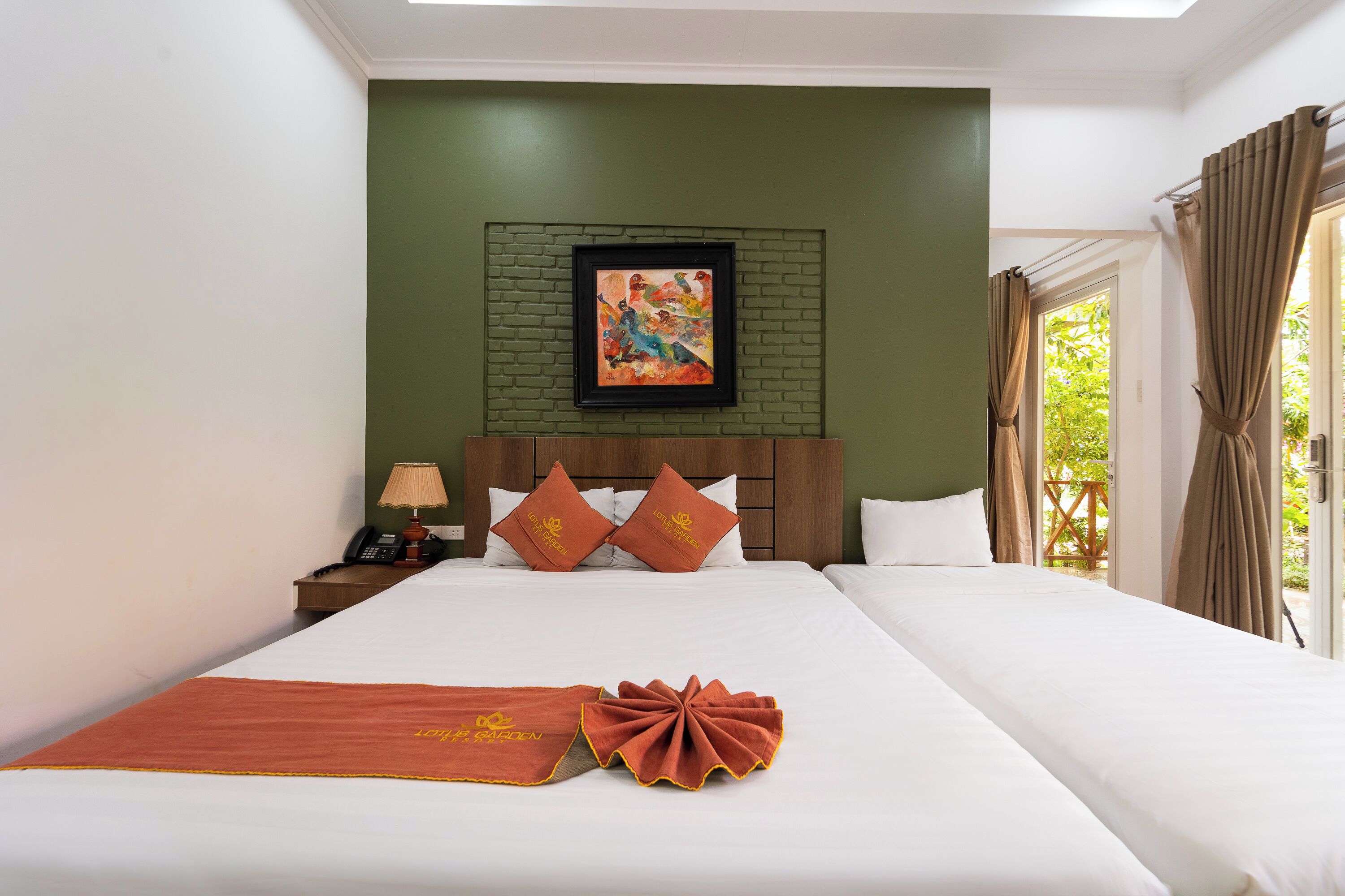 Una habitación de hotel con cama, mesita de noche, teléfono, un cuadro enmarcado en la pared y una ventana con cortinas.