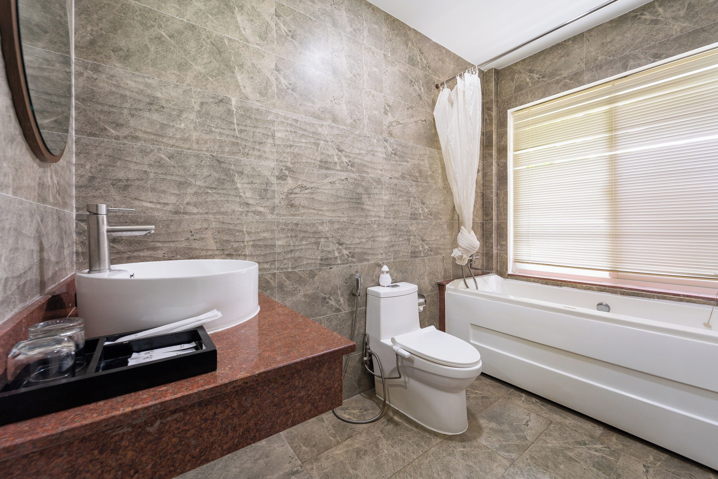A bathroom with a marble wall, a sink, a toilet, and a bathtub.