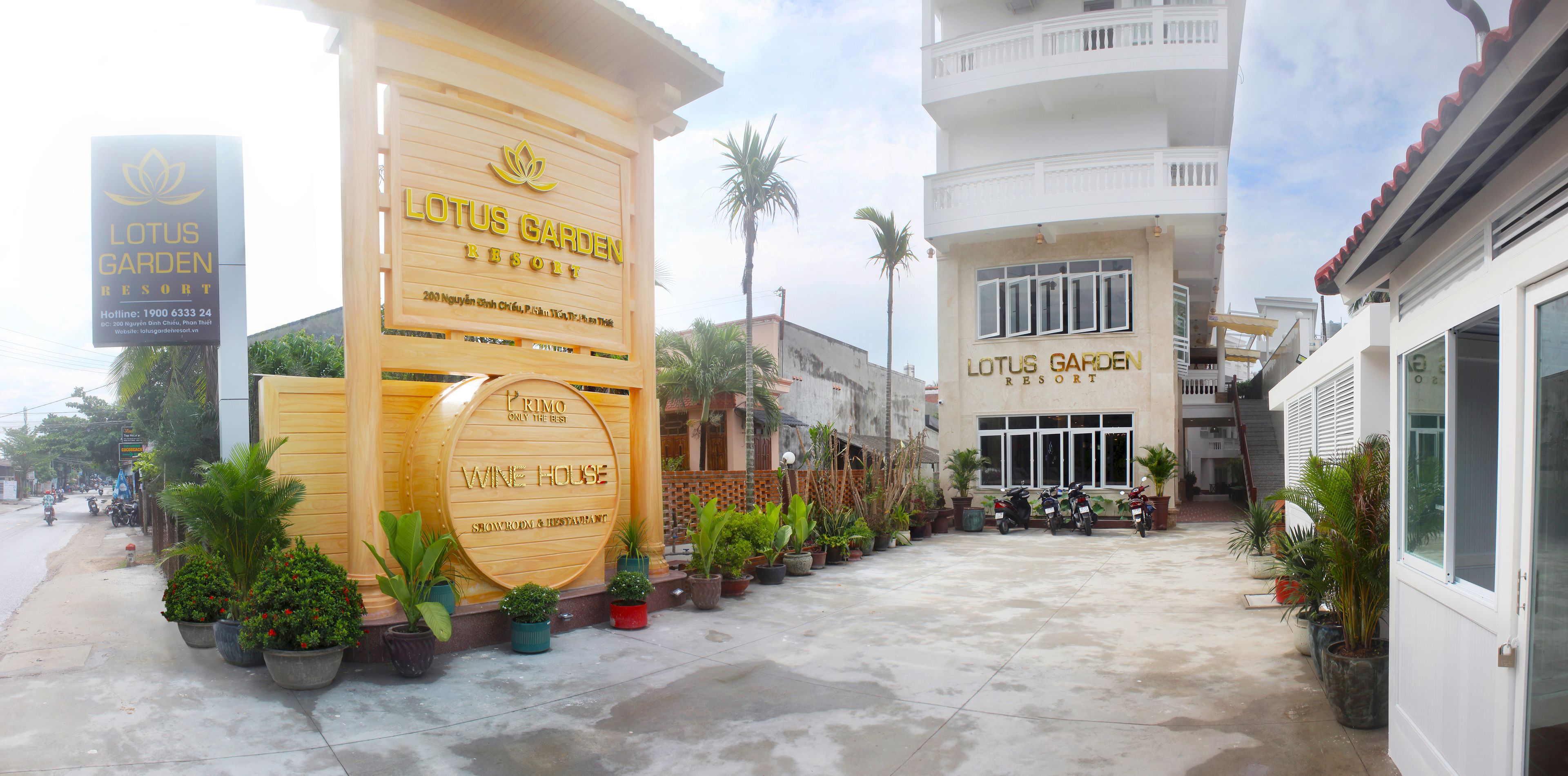 Exterior del Lotus Garden Resort, con un cartel destacado para la Bodega de Vinos, plantas en macetas y motocicletas estacionadas.