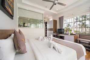 Quarto de hotel com cama, escrivaninha, cadeira, televisão e uma grande janela com vista para palmeiras.