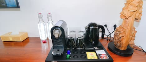 A coffee machine setup with various coffee pods, a tissue box, and a decorative wooden sculpture on a wooden table.