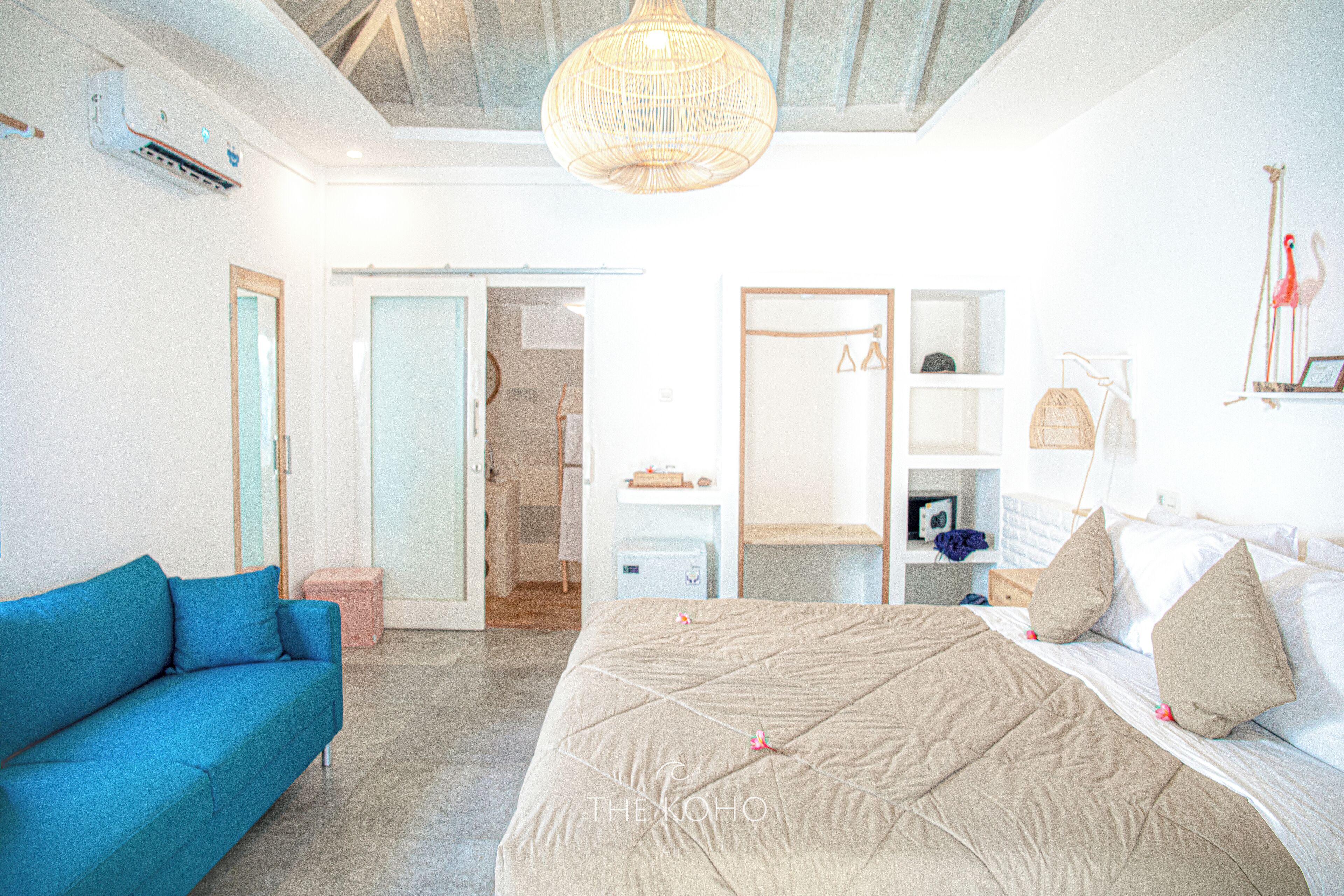 A bedroom with a large bed, a blue sofa, a wardrobe, and a hanging light fixture.