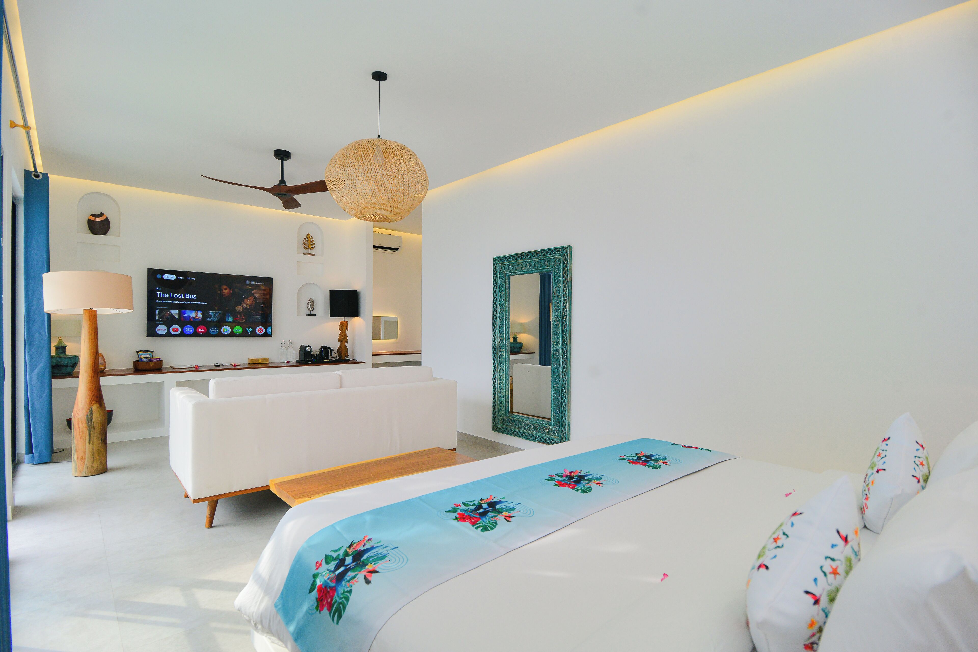 A modern hotel room with a bed, a sofa, a TV, and a ceiling fan.