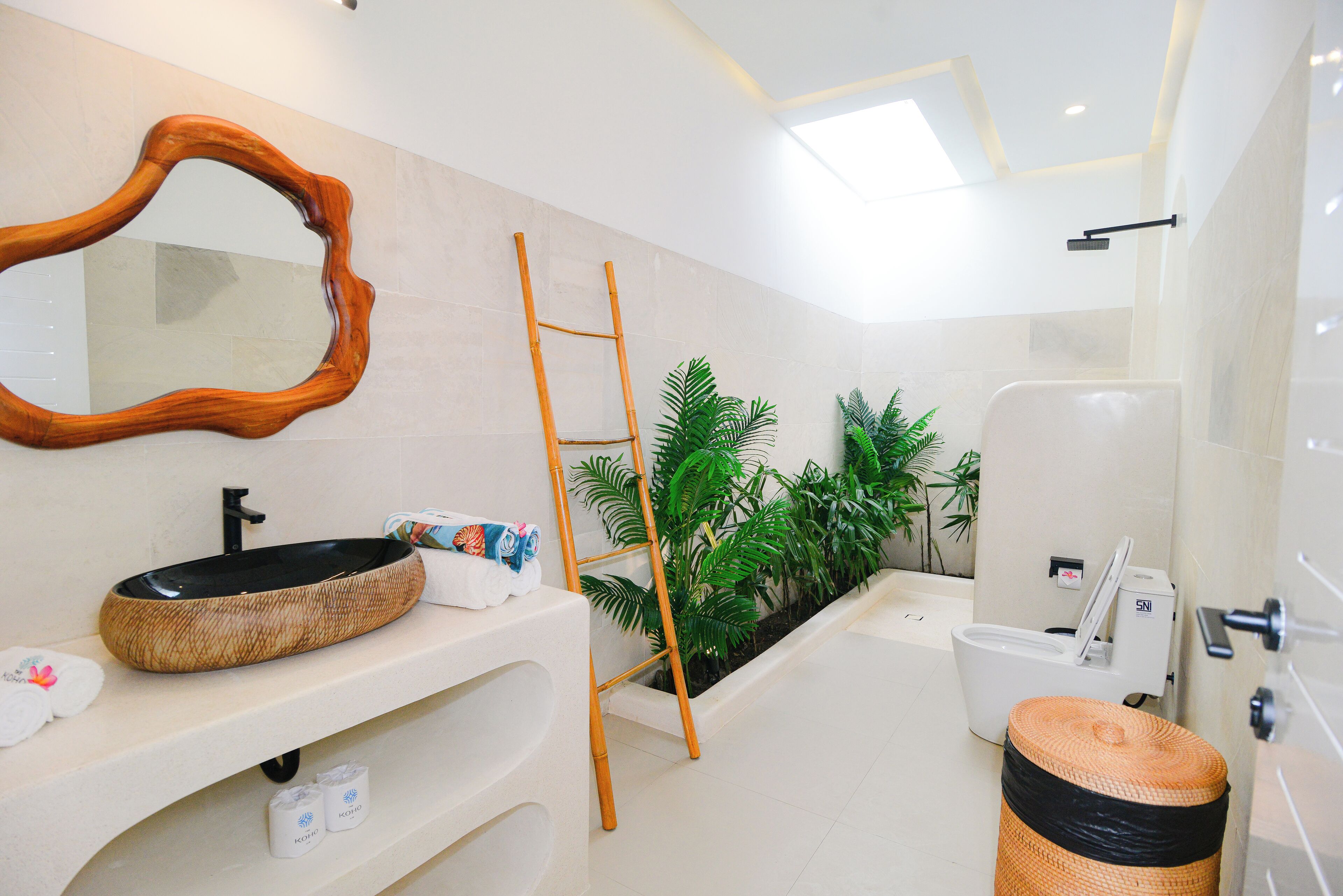 A modern bathroom with a large mirror, a wooden ladder, a sink with a unique bowl design, and a toilet with a bidet attachment.