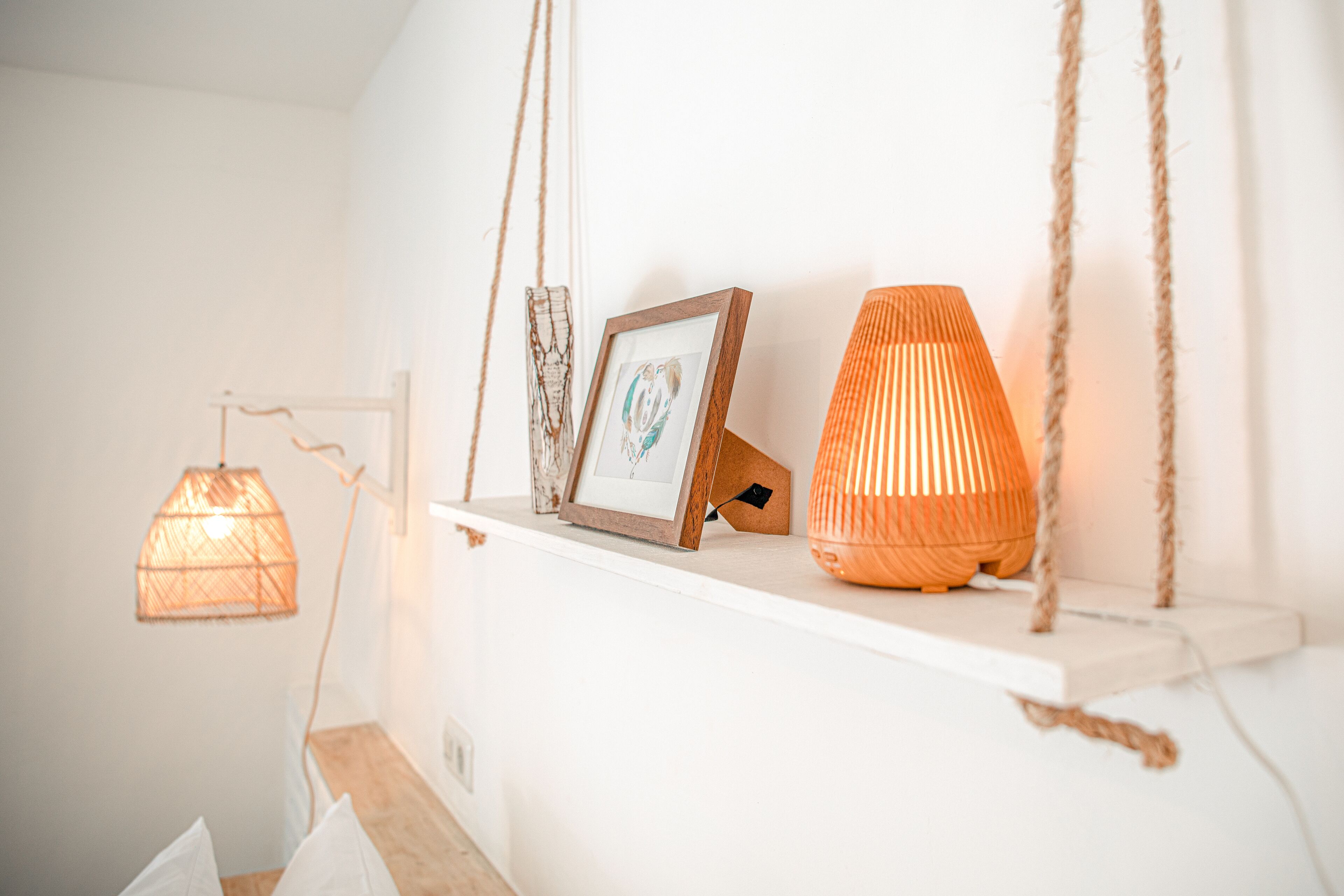 A shelf with a framed picture, a woven lamp, and a candle holder.