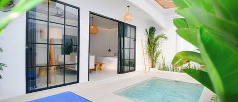 A modern indoor pool area with glass doors leading to a living space, surrounded by plants and a blue mat.