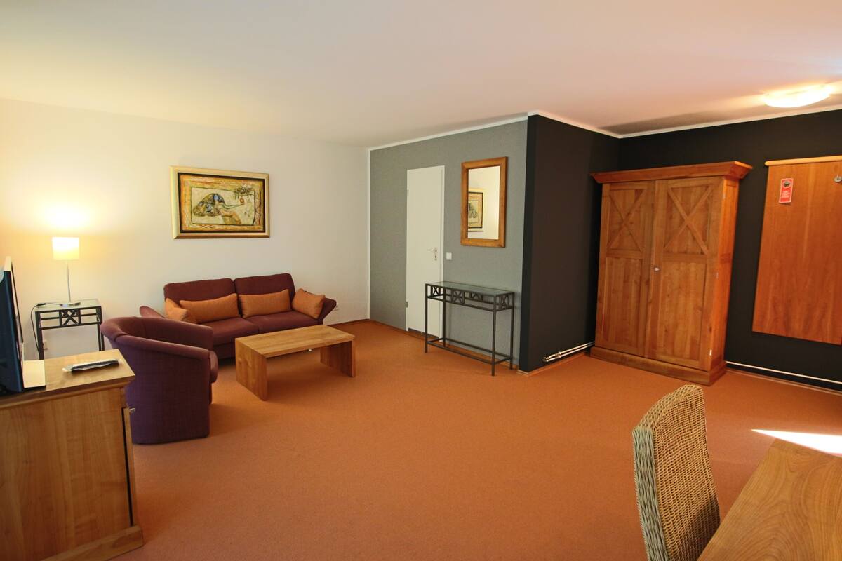 Un salon avec un canapé, une table basse et un meuble pour la télévision. On y trouve également une armoire en bois et un tableau encadré accroché au mur.