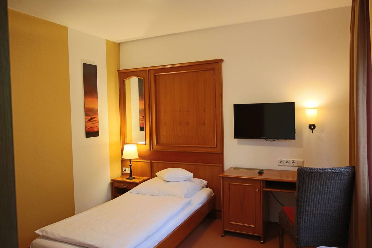 Une chambre d’hôtel équipée d’un lit, d’un bureau, d’une télévision et d’un miroir fixé au mur.
