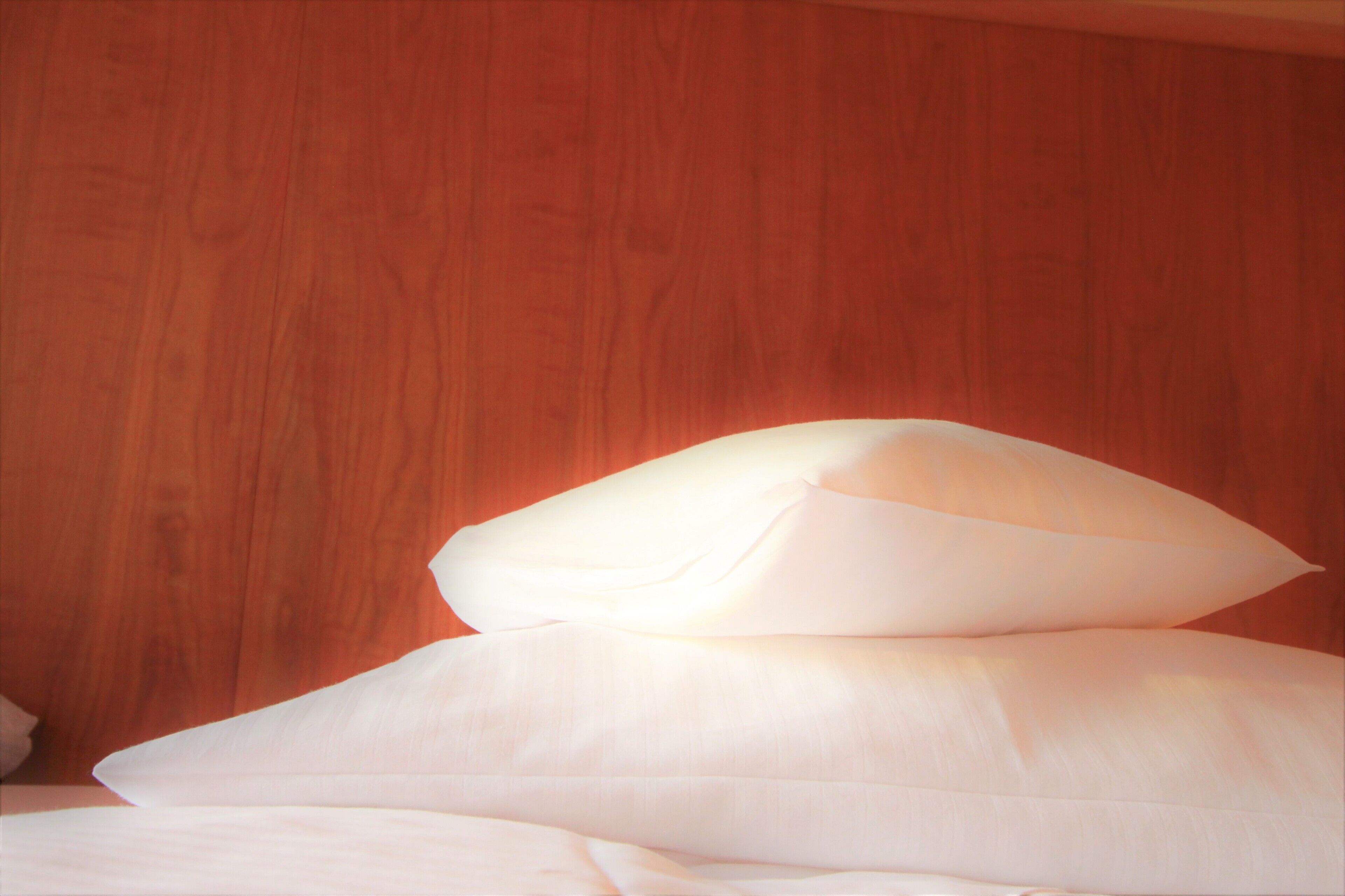 Ein Bett mit weißer Bettwäsche und Kissen an einer Holzwand.