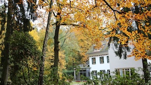 A white house with a balcony, surrounded by trees with yellow leaves.