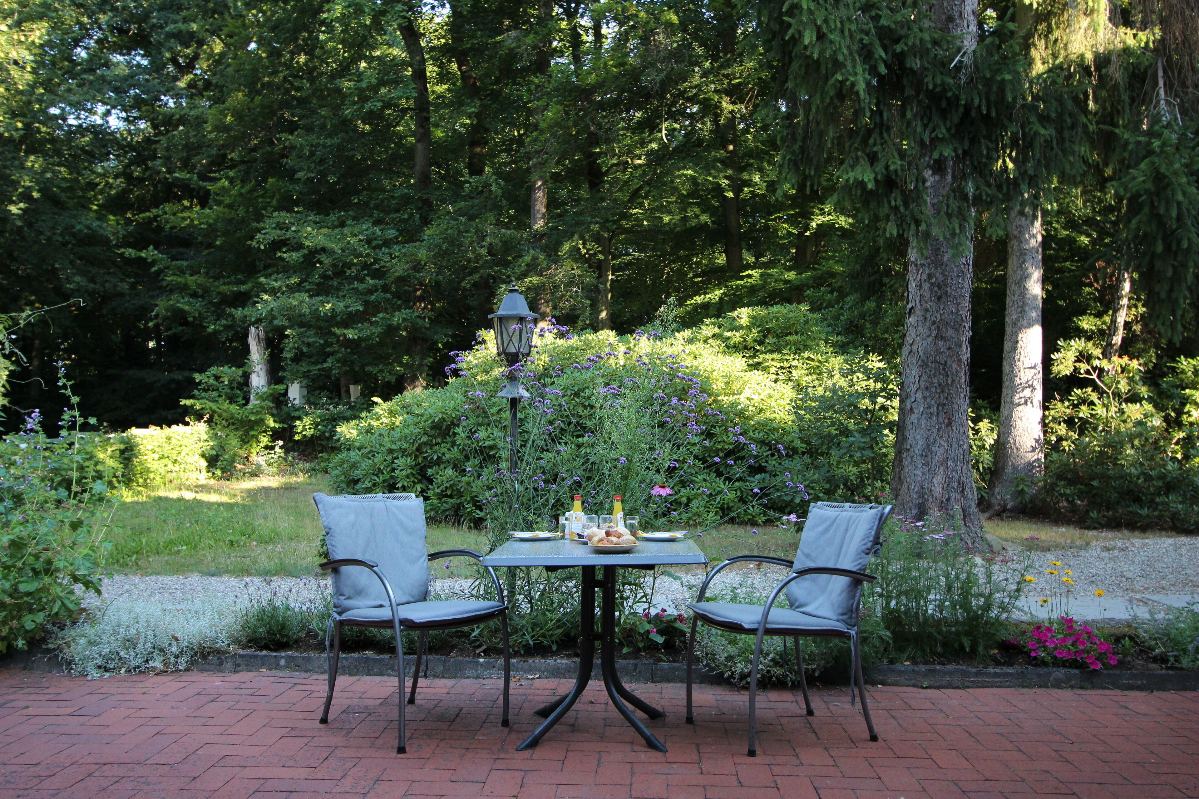 Une terrasse de jardin avec une table et des chaises, entourée d’une végétation luxuriante et d’un lampadaire.