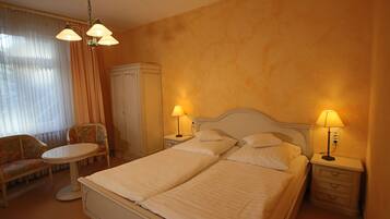 A hotel room with a double bed, two bedside tables with lamps, a chair, a small table, and a wardrobe.
