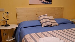 A bedroom with a bed, a nightstand, a lamp, and a painting of a beach scene.