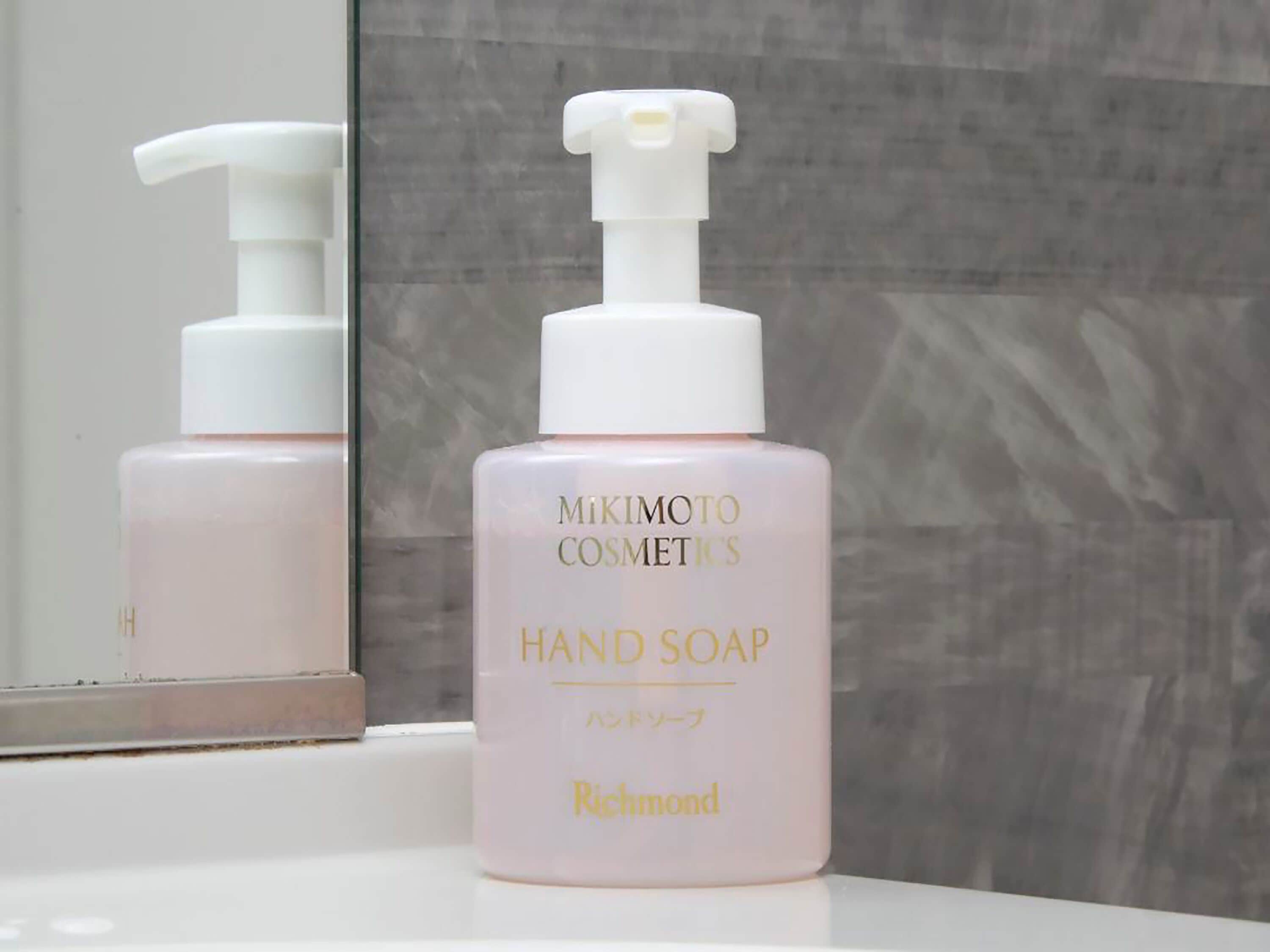 A bottle of MIKIMOTO COSMETICS HAND SOAP with a pump dispenser, placed on a white surface with a mirror reflecting the bottle.