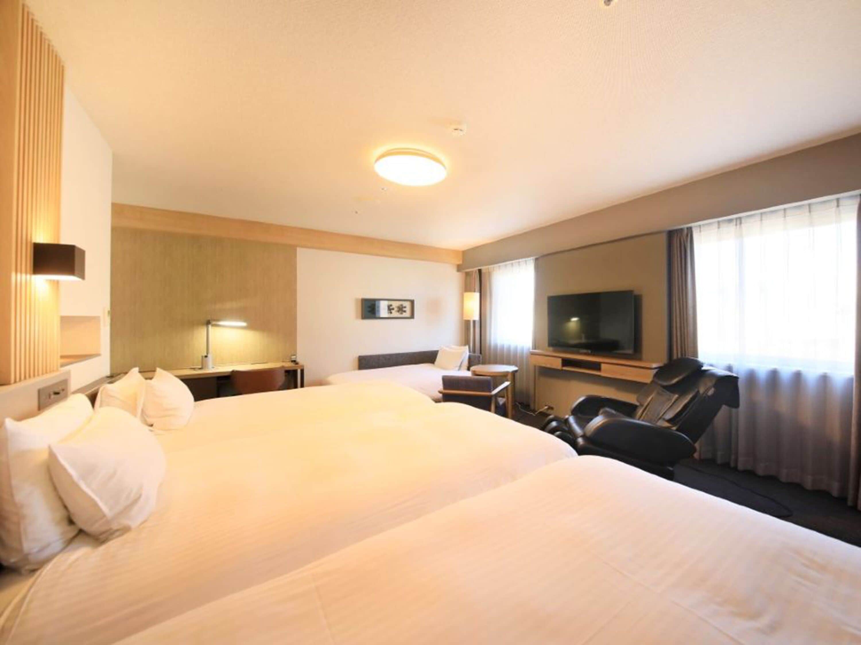 Camera d'albergo con due letti, una scrivania, una sedia, una televisione e un'ampia finestra con tende.