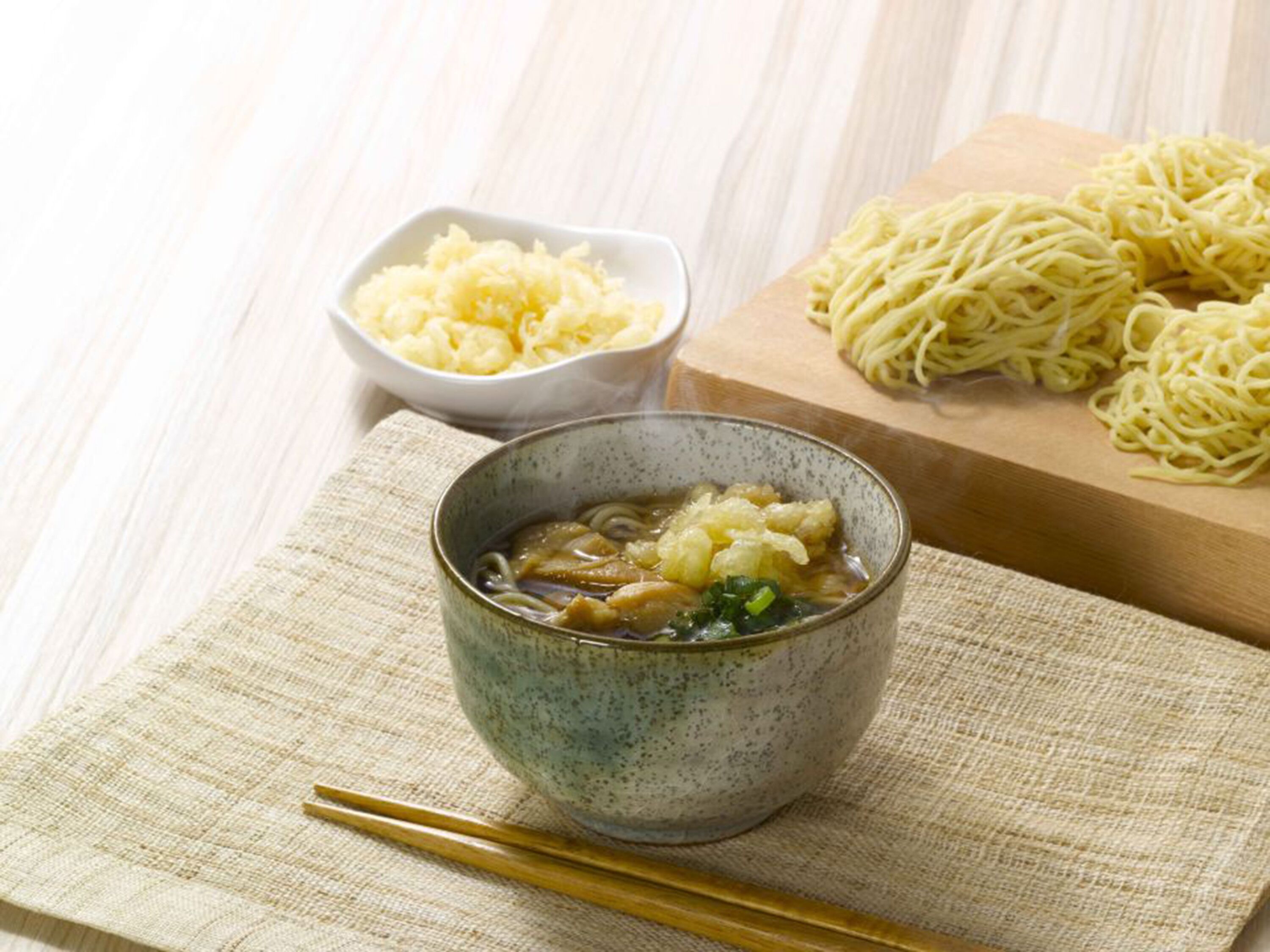 A bowl of ramen with noodles and toppings on a wooden table, accompanied by a bowl of shredded cabbage and a package of ramen noodles.